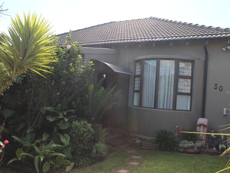 Front facade of a residential house featuring a tiled roof, a curved bay window with security bars, and a small metal entrance awning.