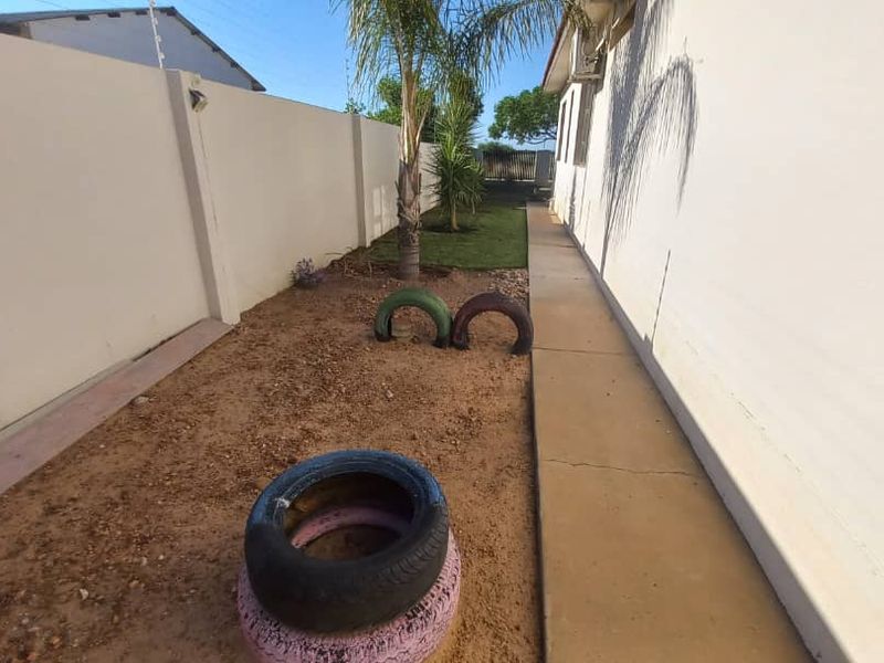 A side exterior area featuring a concrete walkway, perimeter wall with electric fencing, and an external air conditioning unit.