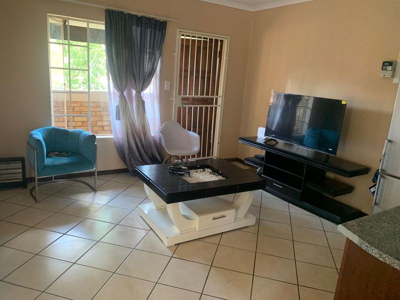 A living room area featuring tiled flooring, a window with security bars, and a security gate leading to the exterior.