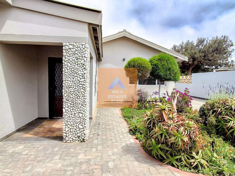Front entrance area featuring a stone-clad pillar, paved walkway, and a tiled porch leading to the main door.
