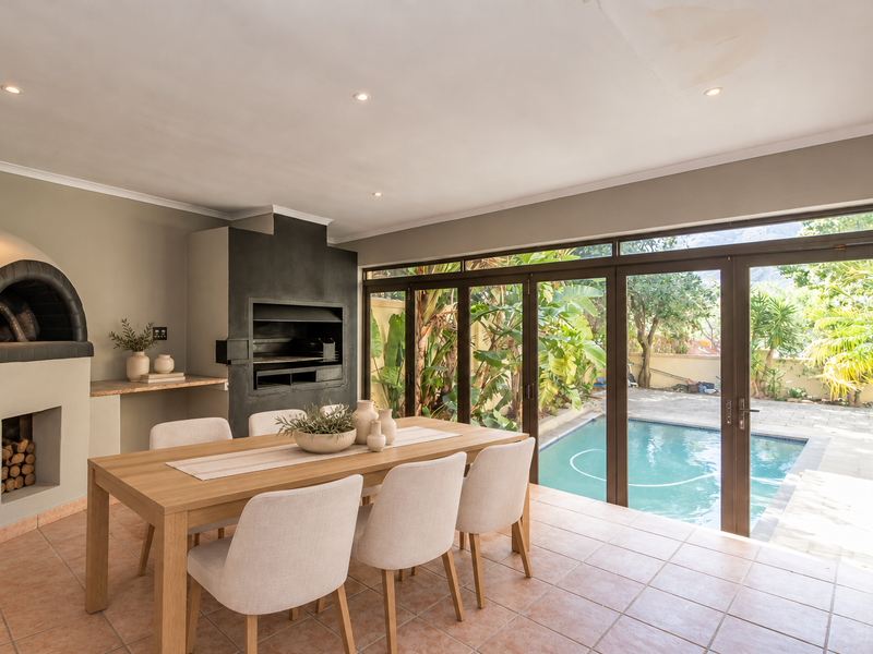 Covered patio area featuring a built-in pizza oven, braai, and large sliding doors opening directly onto the pool deck.