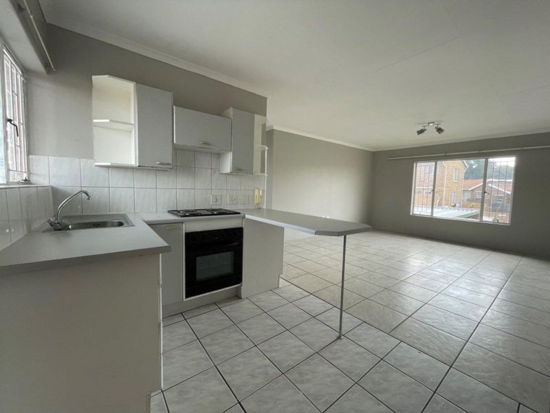 An open-plan kitchen and living area featuring tiled flooring, built-in cabinetry, a breakfast bar, and large windows with security bars.