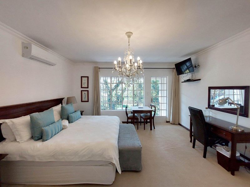 Spacious bedroom featuring a split-system air conditioner, elegant crystal chandelier, crown molding, and large windows providing natural light and access to the outdoors.
