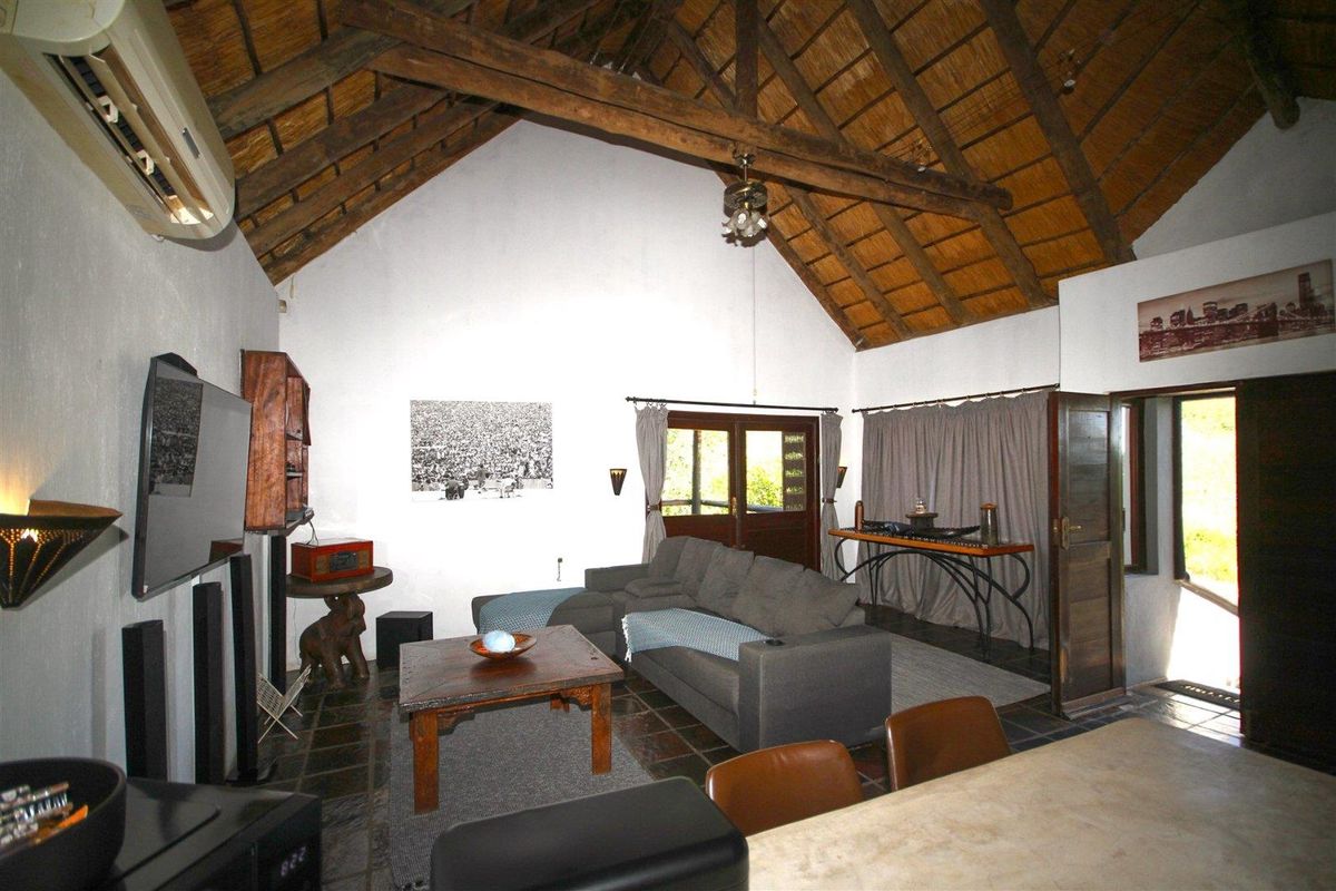 Spacious living area featuring a high vaulted thatched ceiling with exposed timber beams, tiled flooring, and direct access to an outdoor patio.