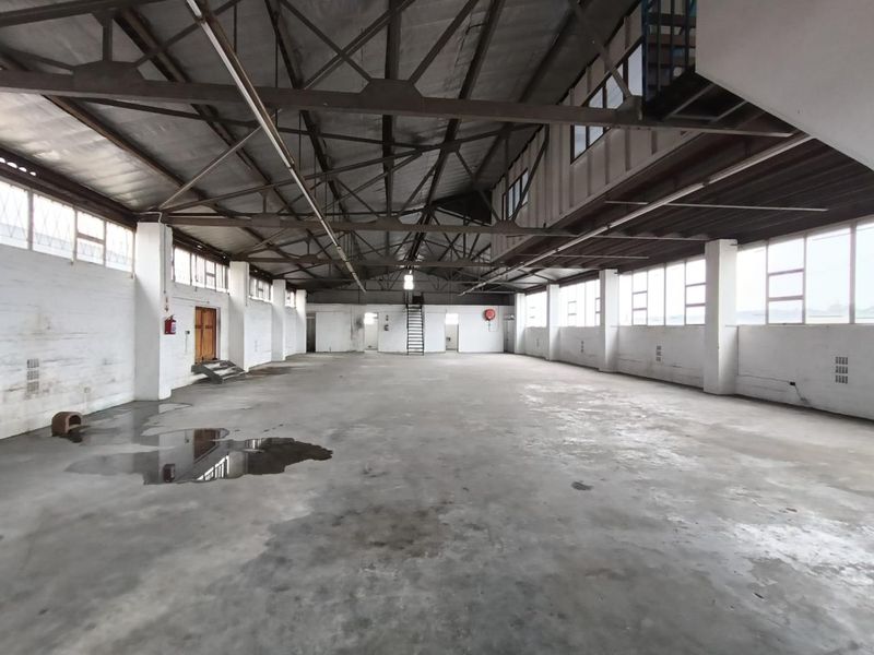 Spacious industrial warehouse unit featuring high ceilings with exposed steel trusses, concrete flooring, and large windows providing ample natural light.
