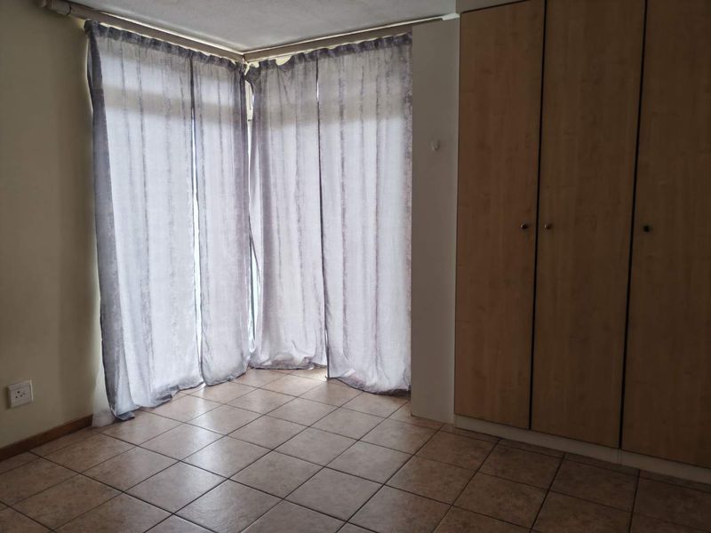 A bright, empty bedroom featuring tiled flooring and built-in wooden cupboards, offering a clean and functional space ready for personalization.