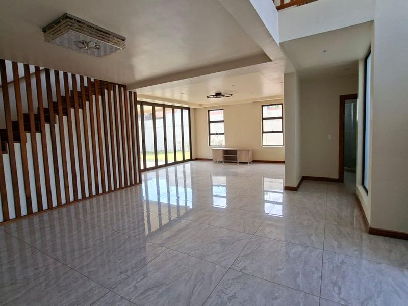 Spacious, modern open-plan living area featuring polished tile flooring, a striking timber staircase screen, and large bi-fold doors opening to the rear garden.