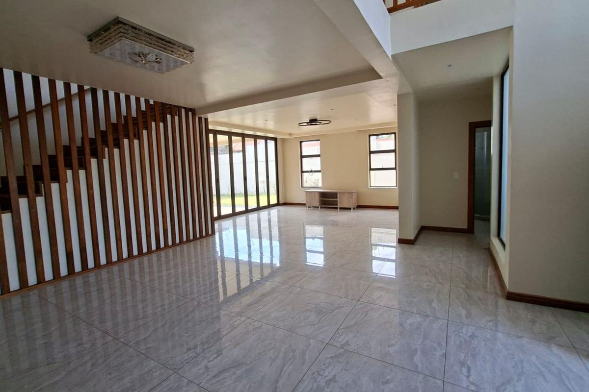 Spacious, modern open-plan living area featuring polished tile flooring, a striking timber staircase screen, and large bi-fold doors opening to the rear garden.