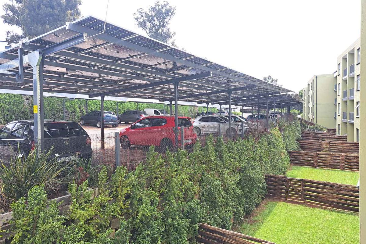 Exterior view of the apartment complex featuring a covered parking area with integrated solar panels and landscaped garden spaces.