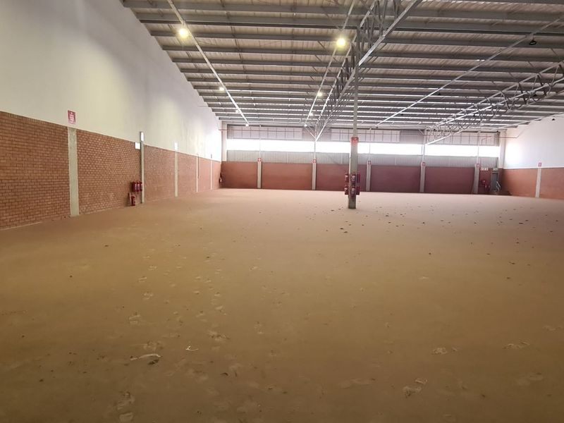 A large, open-plan industrial warehouse space featuring exposed brick walls, high-clearance steel truss roofing, and polished concrete flooring.