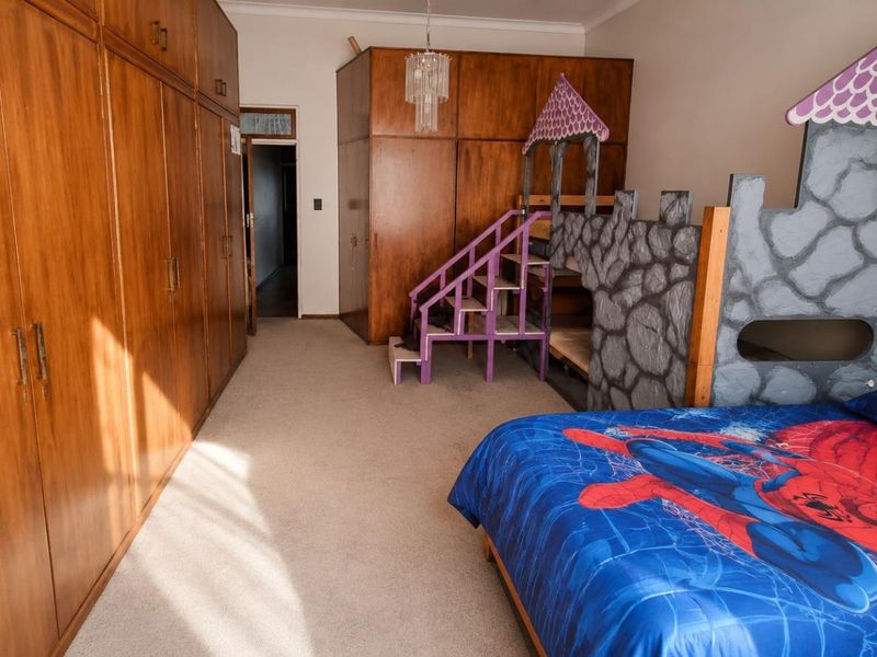 A spacious bedroom featuring extensive wall-to-wall built-in wooden cupboards and neutral carpeting, offering ample storage space.