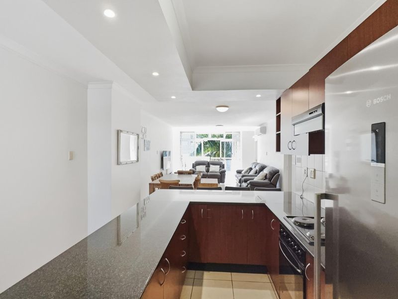 Open-plan kitchen and living area featuring granite countertops, built-in cabinetry, and tiled flooring, leading to a bright living space.