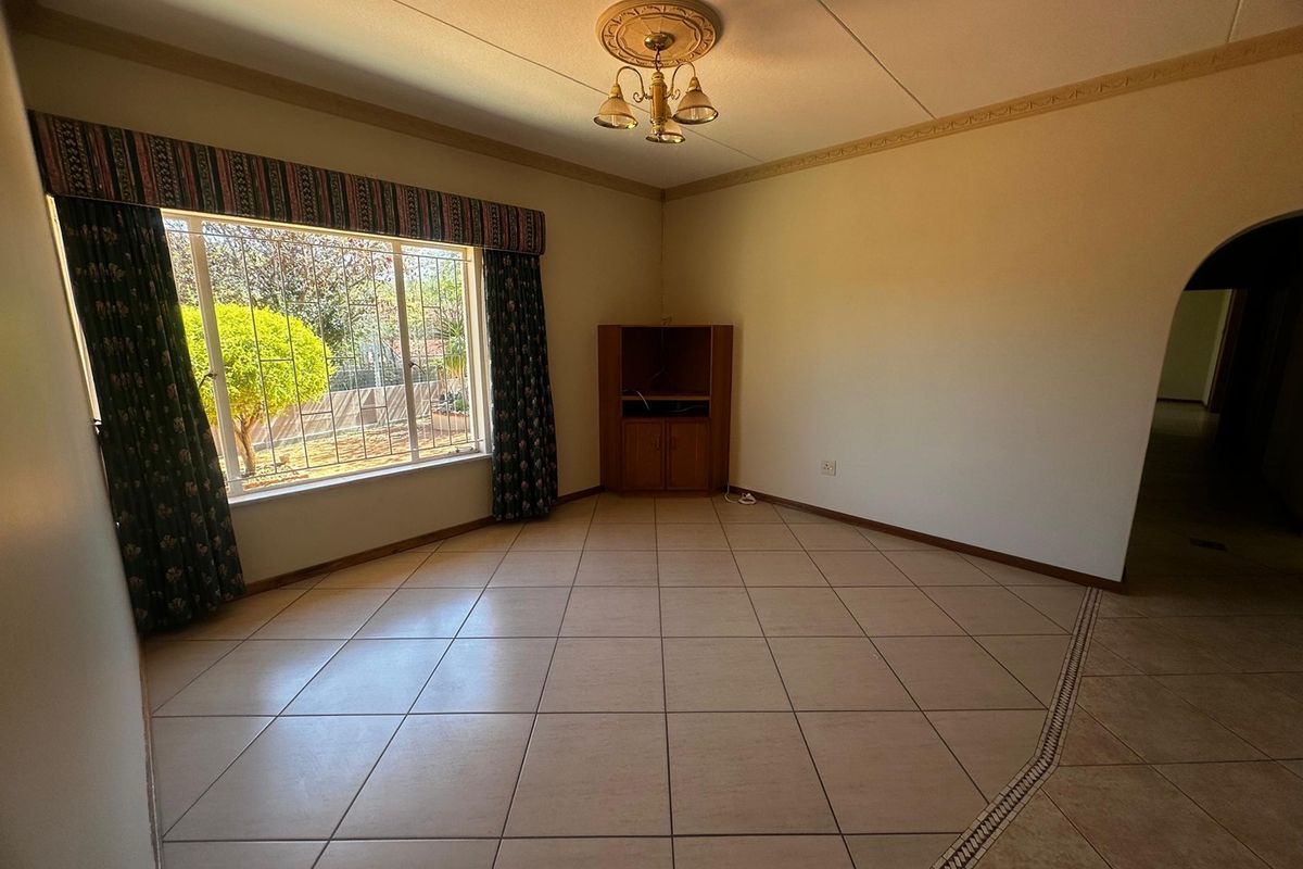 A spacious, empty living room featuring ceramic floor tiles, a decorative ceiling rose, and an arched entryway, offering a blank canvas for interior design.