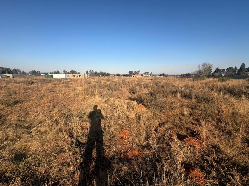 A wide-angle view of a vacant residential plot featuring dry grass and surrounding perimeter fencing.