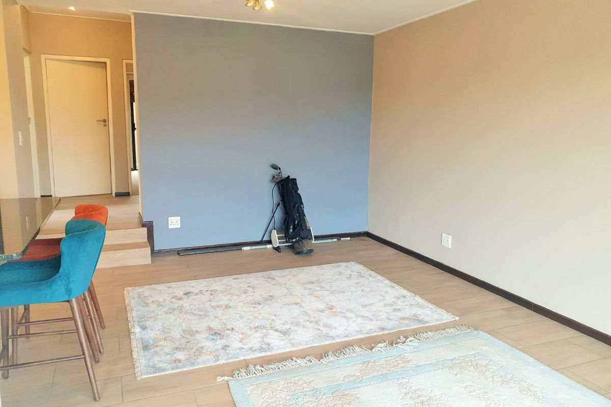 A spacious, open-plan living area featuring neutral-toned walls, tiled flooring, and a modern accent wall, providing a versatile space for interior design.