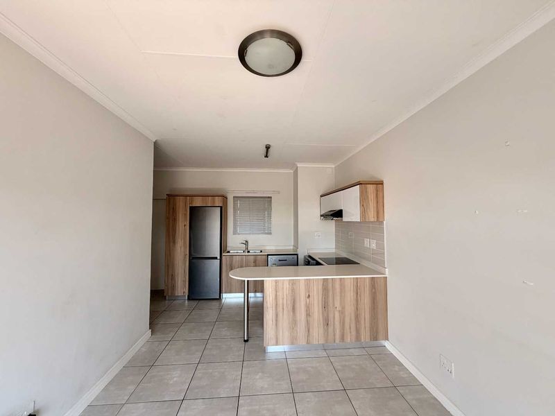 An open-plan kitchen area featuring modern wood-finish cabinetry, a breakfast bar, tiled flooring, and integrated cooking appliances in a clean, vacant space.