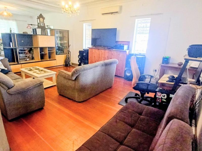 Spacious living room featuring polished hardwood flooring, ornate ceiling detailing, and a wall-mounted split-system air conditioner.