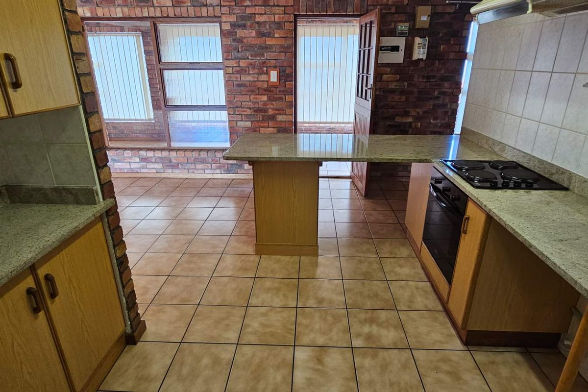 Kitchen featuring granite countertops, built-in oven and hob, tiled flooring, and exposed brick walls with an integrated breakfast bar area.