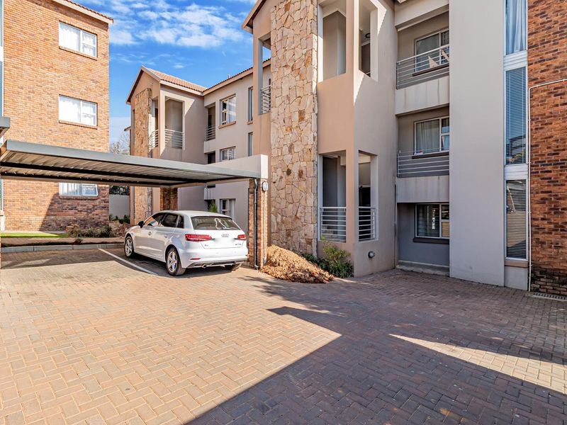 Exterior view of an apartment complex featuring a covered parking bay, brick paving, and stone-clad architectural details.