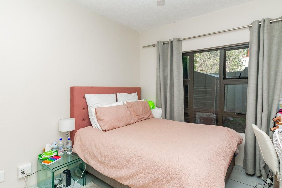 A functional bedroom featuring neutral walls, tiled flooring, and a large window with curtain rod, providing natural light and access to the exterior.