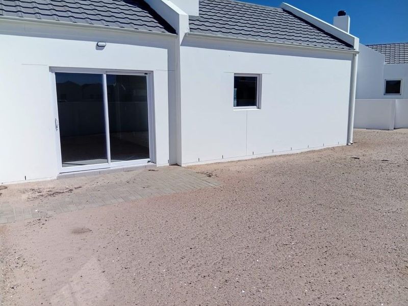 Rear view of the property featuring a paved patio area, sliding glass doors, and a clean white exterior finish with a tiled roof.