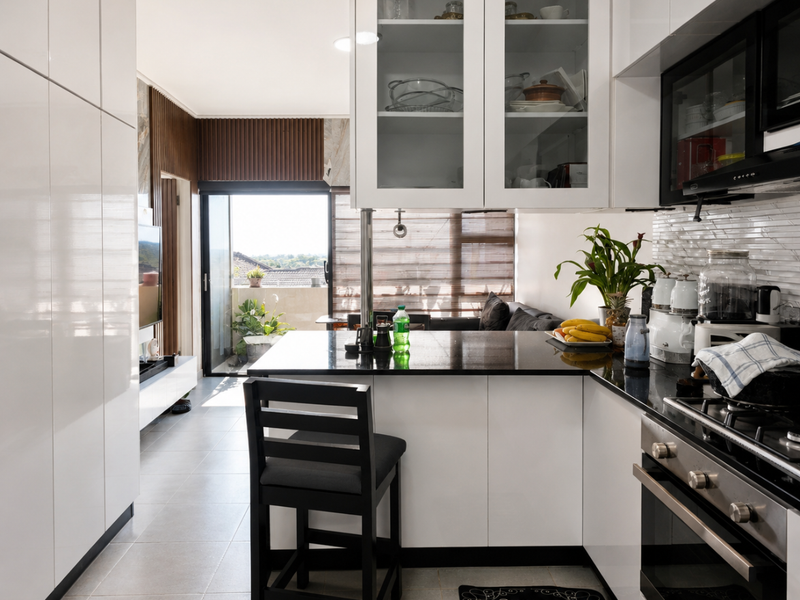 Modern open-plan kitchen featuring high-gloss white cabinetry, black granite countertops, integrated appliances, and seamless flow to an adjoining balcony area.