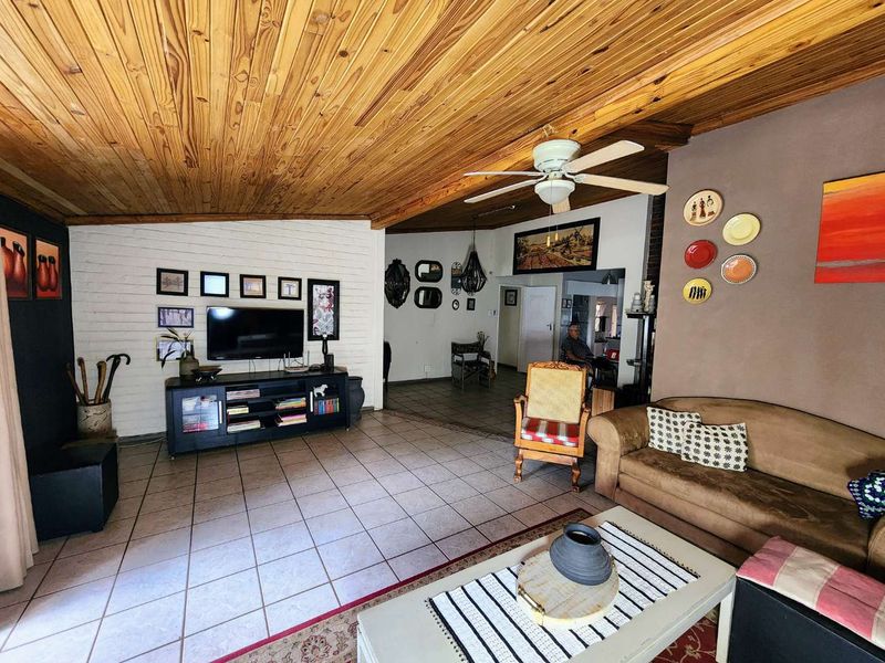Spacious living room featuring a warm timber-clad ceiling, tiled flooring, and a painted brick feature wall, creating a comfortable and inviting atmosphere.