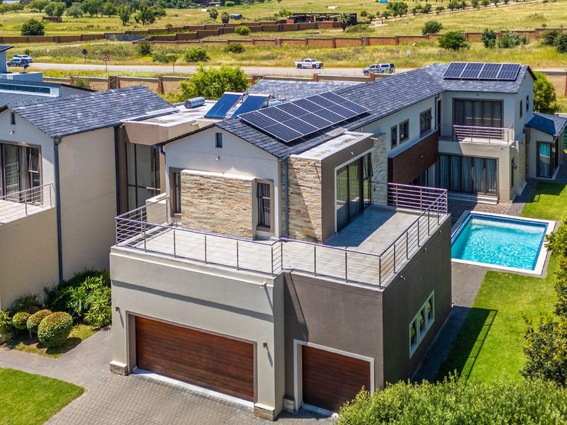 Aerial view of a modern multi-story residential property featuring solar panels, a swimming pool, paved driveway, and multiple balconies.