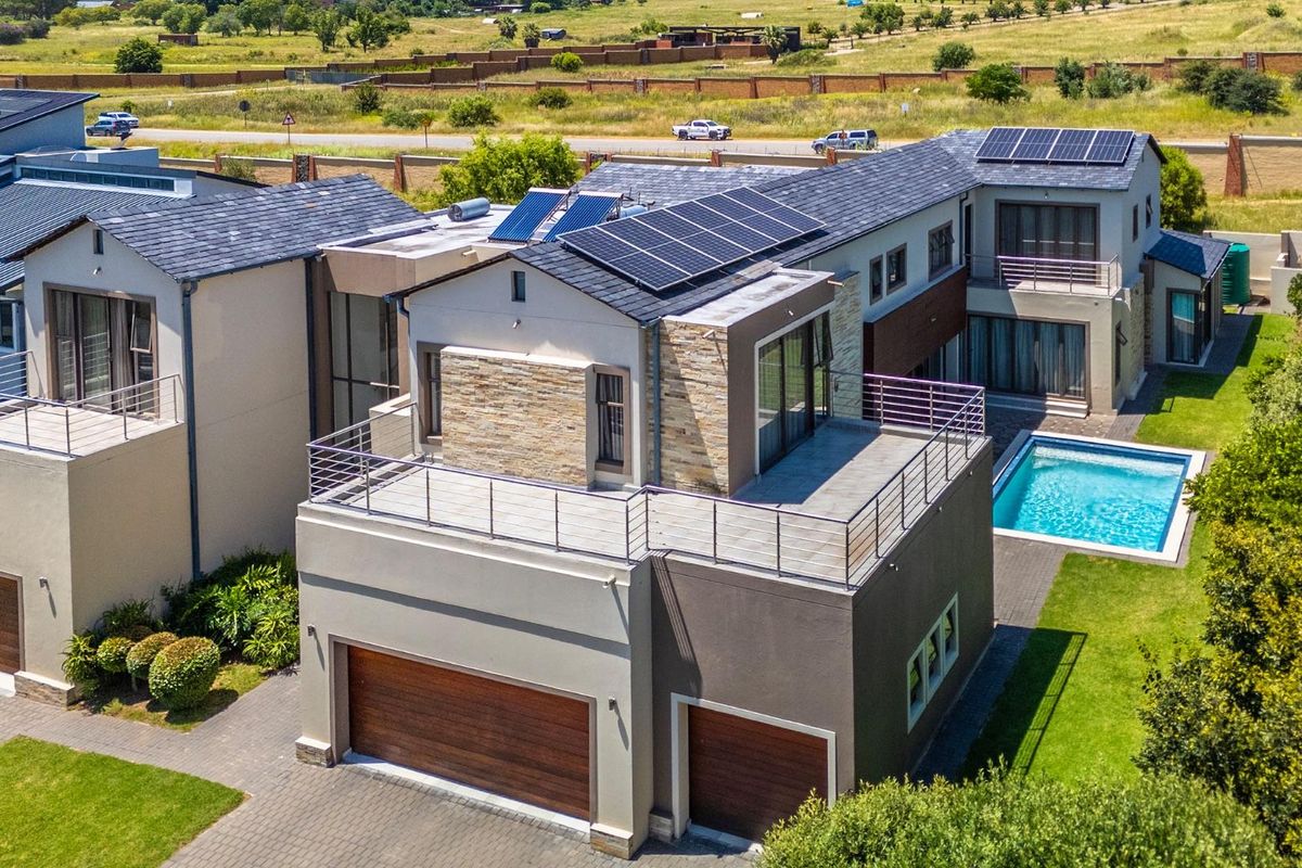Aerial view of a modern multi-story residential property featuring solar panels, a swimming pool, paved driveway, and multiple balconies.