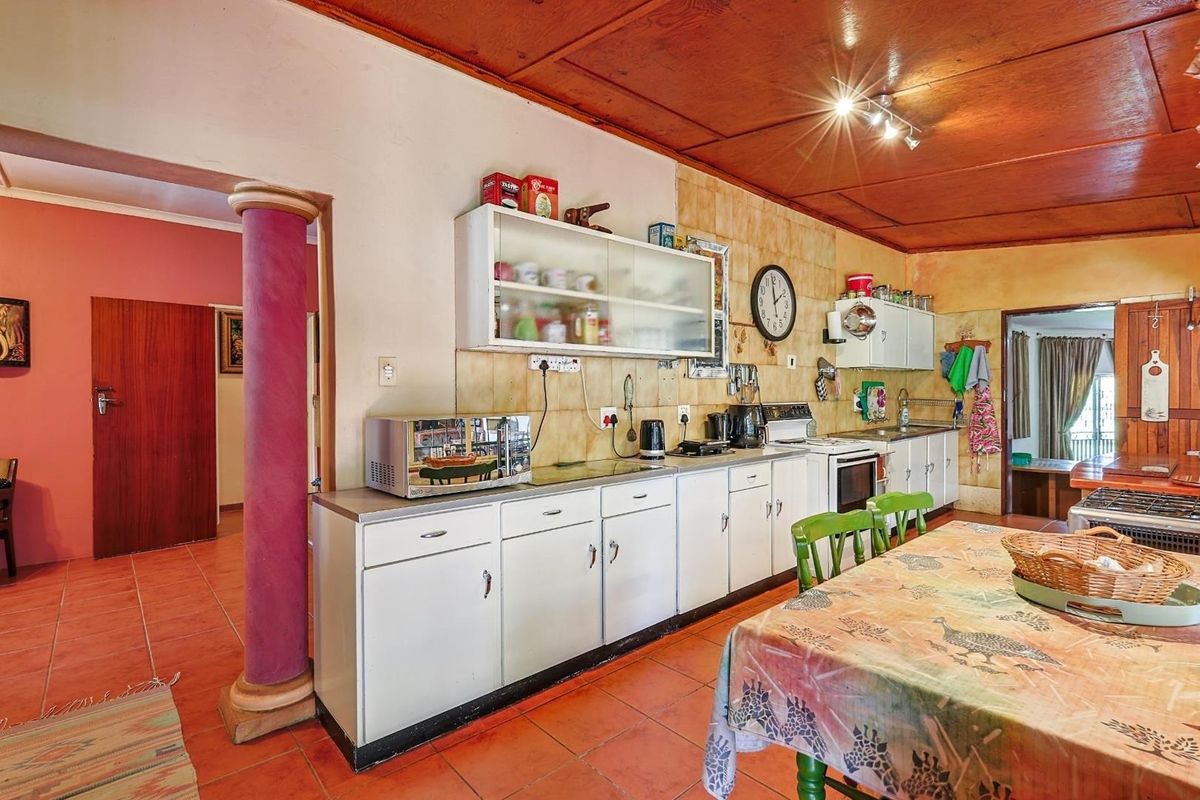 A dated kitchen area featuring white cabinetry, tiled backsplash, and a wooden ceiling, with an open-plan layout connecting to adjacent living spaces.