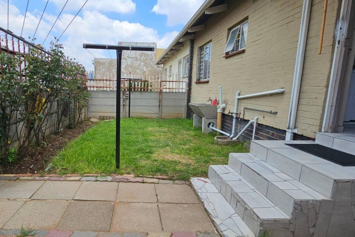 Rear exterior view of the property featuring a small lawn, paved area, concrete wash basin, and external staircase access.
