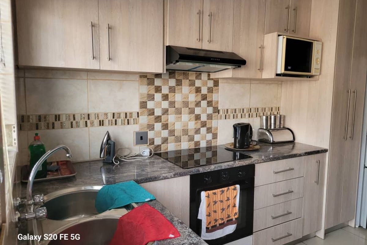 A functional kitchen featuring light wood-grain cabinetry, granite-look laminate countertops, a built-in oven with ceramic hob, and a tiled splashback.