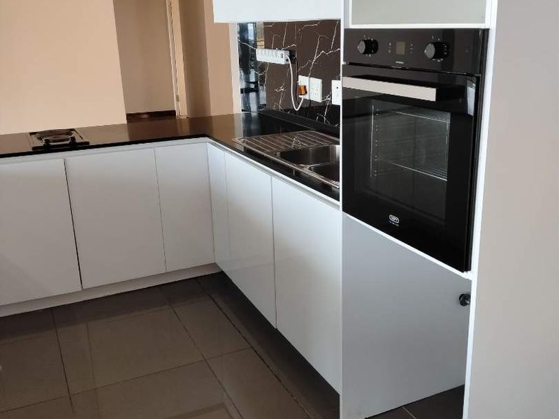 Modern kitchen featuring glossy white cabinetry, black stone countertops, marble-effect splashback, and a built-in oven with sleek ceramic floor tiling.