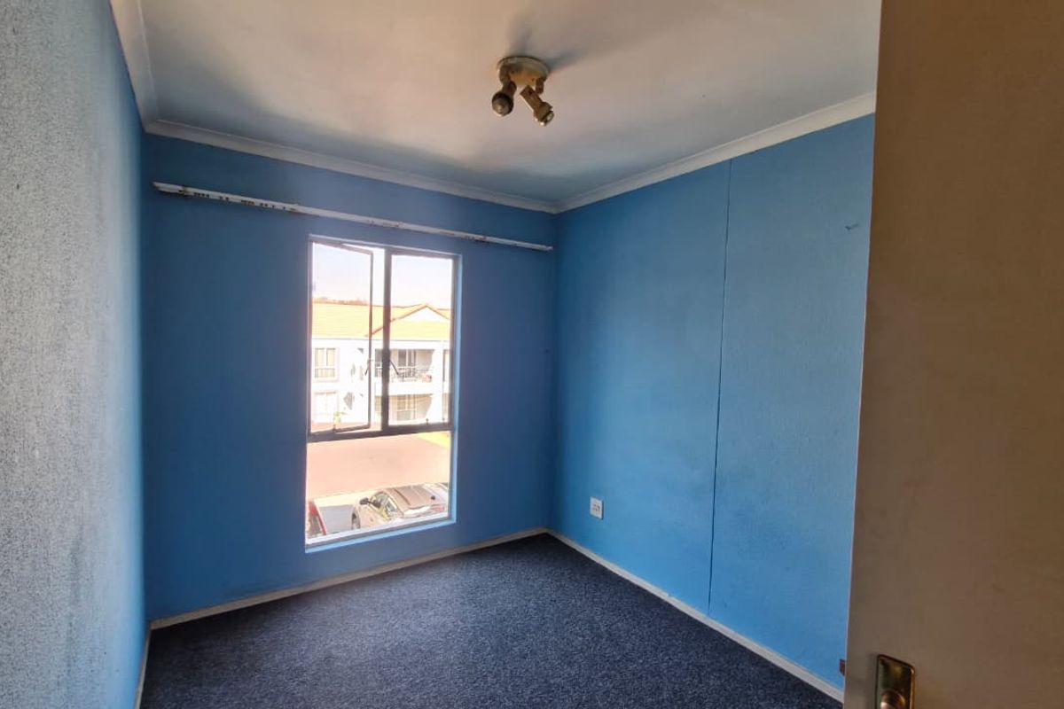 An empty bedroom featuring blue painted walls, carpet flooring, and a large window, offering a blank canvas for potential renovation or restyling.