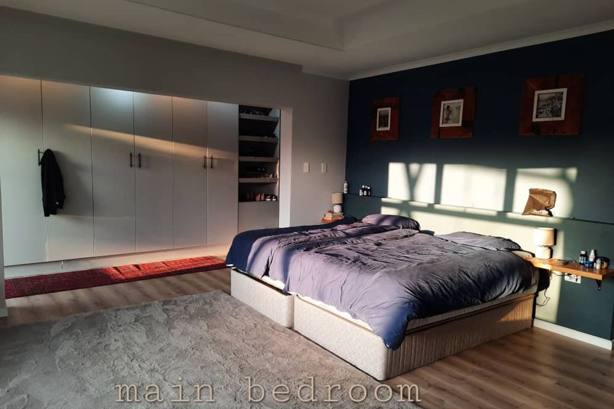 Spacious main bedroom featuring extensive built-in cabinetry, modern laminate flooring, and a striking dark blue accent wall.