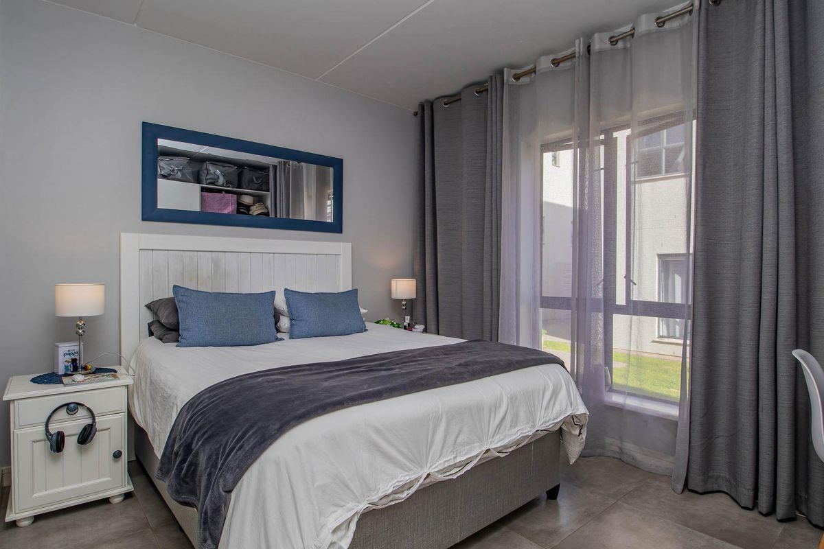 A well-maintained bedroom featuring large windows with floor-to-ceiling curtains, neutral wall tones, and tiled flooring.