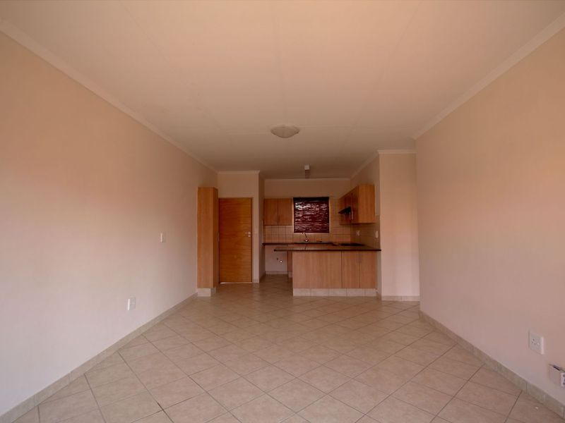 An open-plan living and kitchen area featuring tiled flooring, neutral walls, and functional built-in cabinetry with a breakfast bar.
