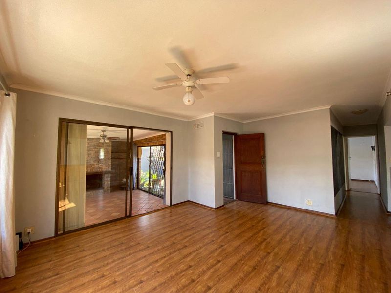 Spacious living room featuring laminate flooring, a ceiling fan, and sliding glass doors providing access to an outdoor patio area.