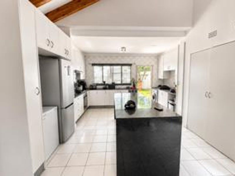Spacious kitchen featuring a central island with granite countertops, ample built-in cabinetry, tiled flooring, and exposed timber ceiling beams.