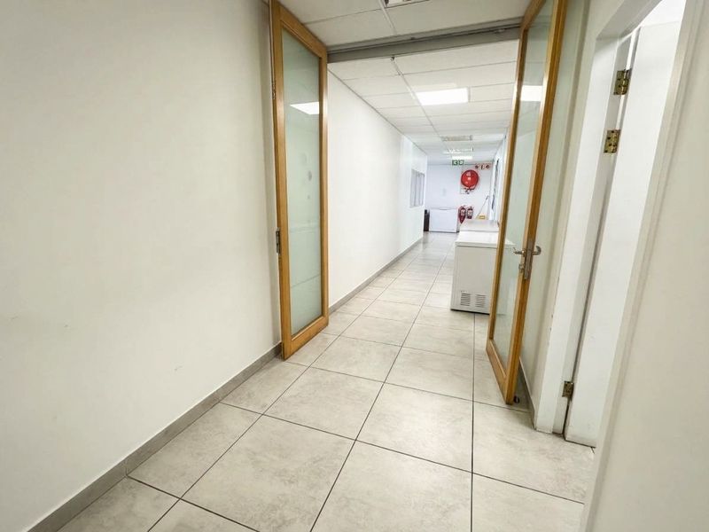 A functional commercial hallway featuring tiled flooring, suspended ceiling panels, and double glass doors leading to an adjacent utility area.