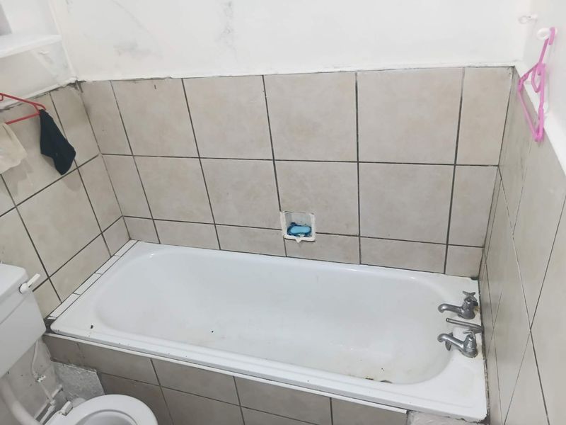 A functional bathroom featuring a standard bathtub with wall tiling and basic fixtures, currently requiring maintenance and cosmetic updates.