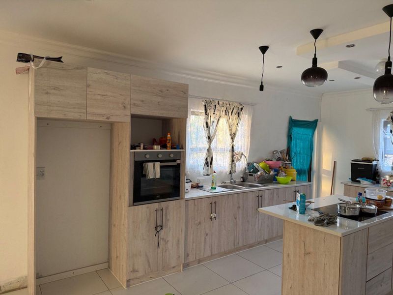 Modern kitchen featuring light wood-grain cabinetry, stone countertops, a central island, built-in oven, and tiled flooring with contemporary pendant lighting.