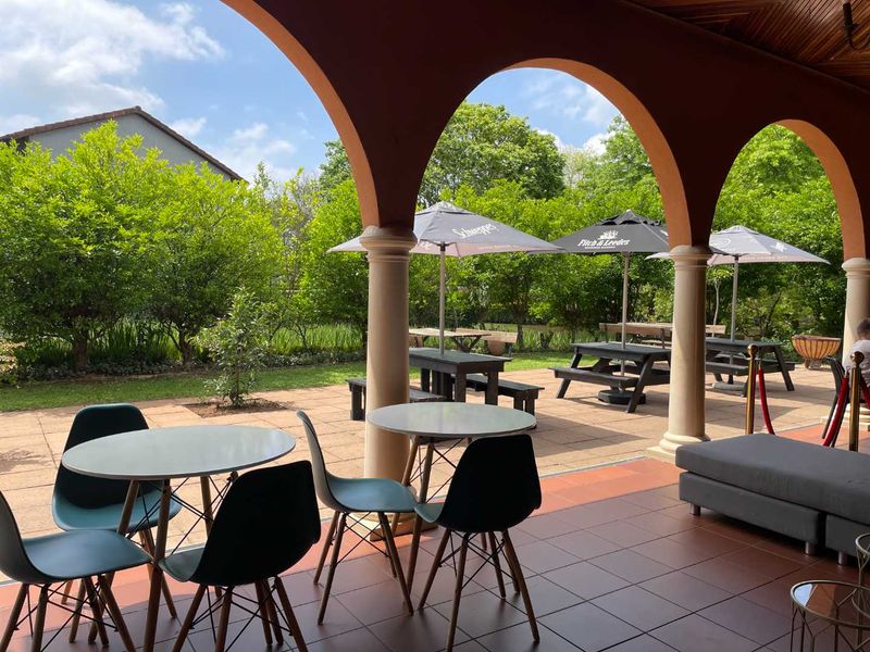 A spacious covered patio featuring arched columns, tiled flooring, and a timber ceiling, overlooking a landscaped garden area.