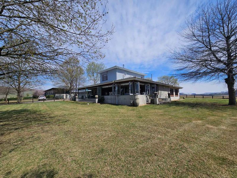 A view of the rear elevation of the farmhouse, featuring a covered patio with bi-fold doors and expansive surrounding lawn.