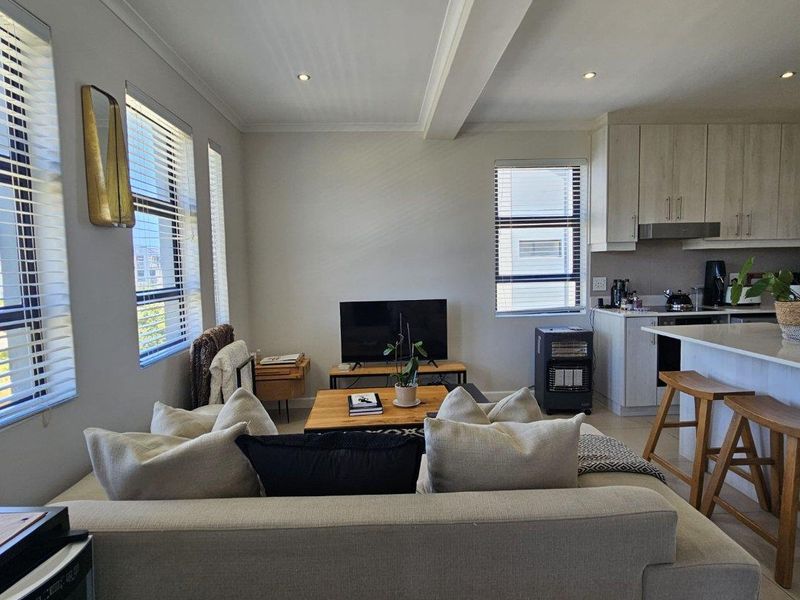 Open-plan living area featuring a modern kitchen with stone countertops, integrated cabinetry, and recessed lighting, seamlessly flowing into a bright, comfortable lounge space.