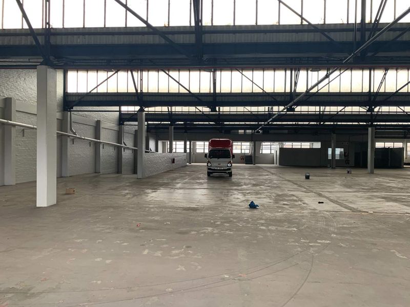 Spacious industrial warehouse featuring high ceilings with exposed steel trusses, clerestory windows for natural light, and durable concrete flooring.