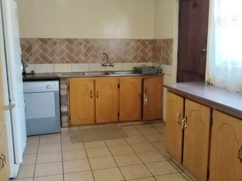 A functional kitchen featuring wooden cabinetry, tiled backsplash, and tiled flooring, offering a dated aesthetic with potential for modern renovation.