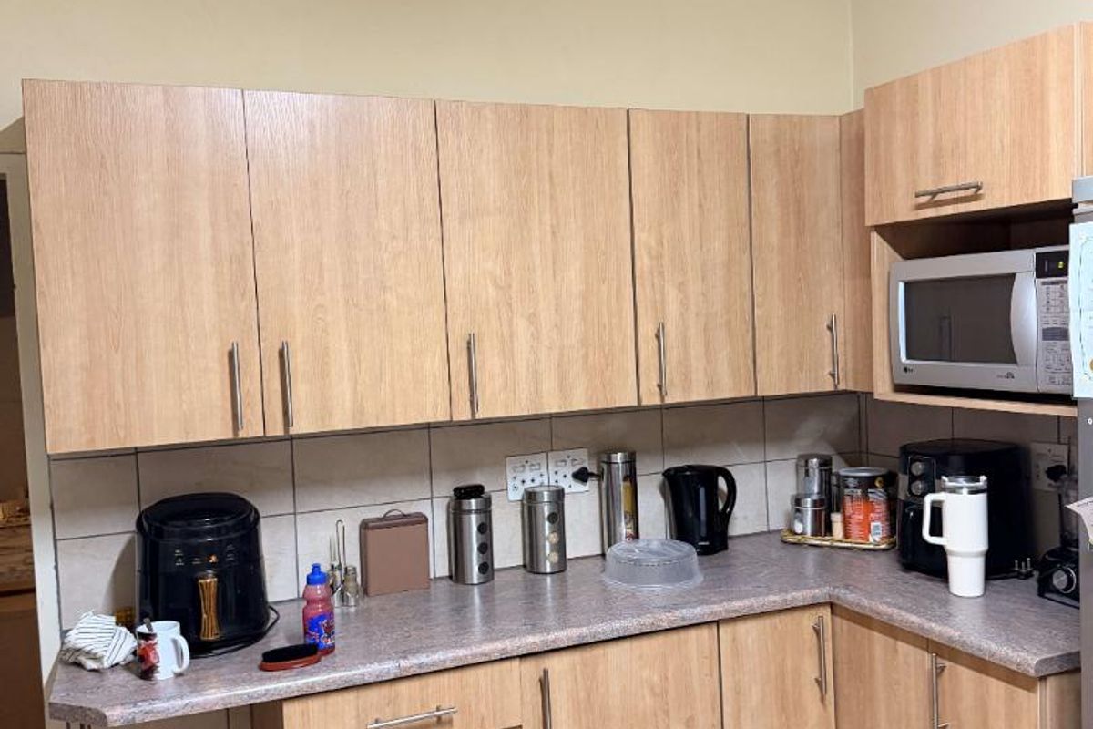 A functional kitchen featuring light wood-look cabinetry, laminate countertops, tiled splashbacks, and built-in microwave housing.
