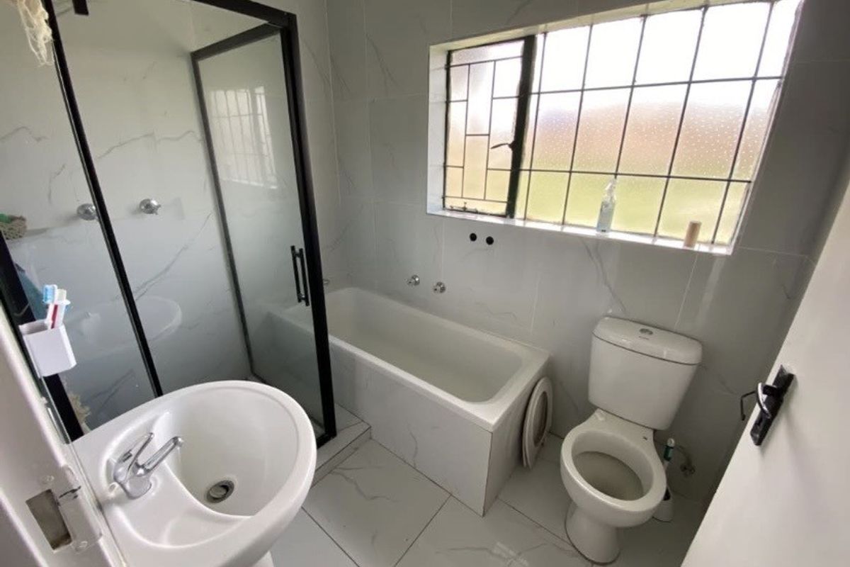 A modern bathroom featuring a pedestal basin, a separate shower enclosure with black framing, a bathtub, and a toilet, finished with light-toned marble-look tiles.