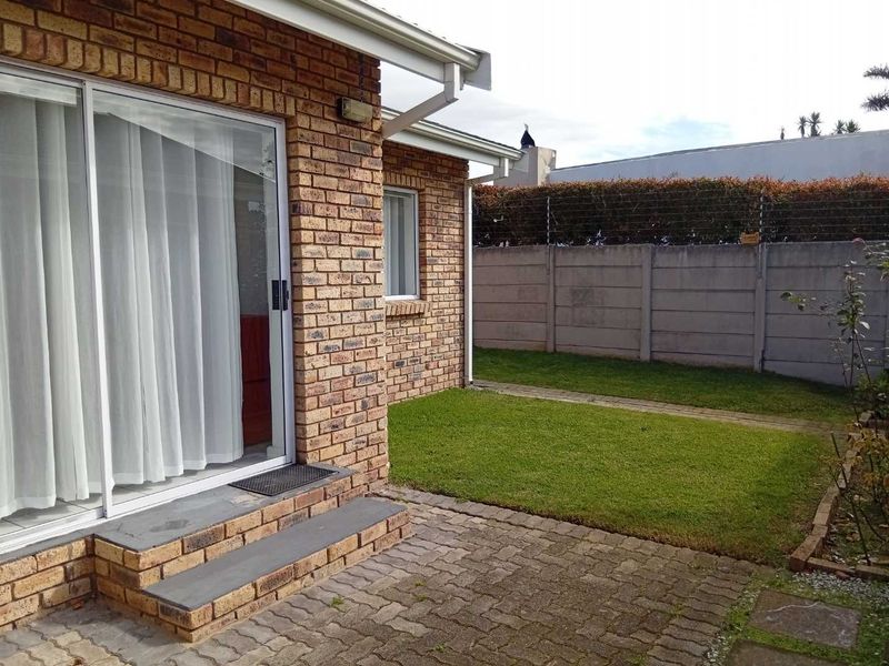 Rear exterior view of the townhouse featuring a face brick facade, paved patio area, and a private garden enclosed by a precast boundary wall.